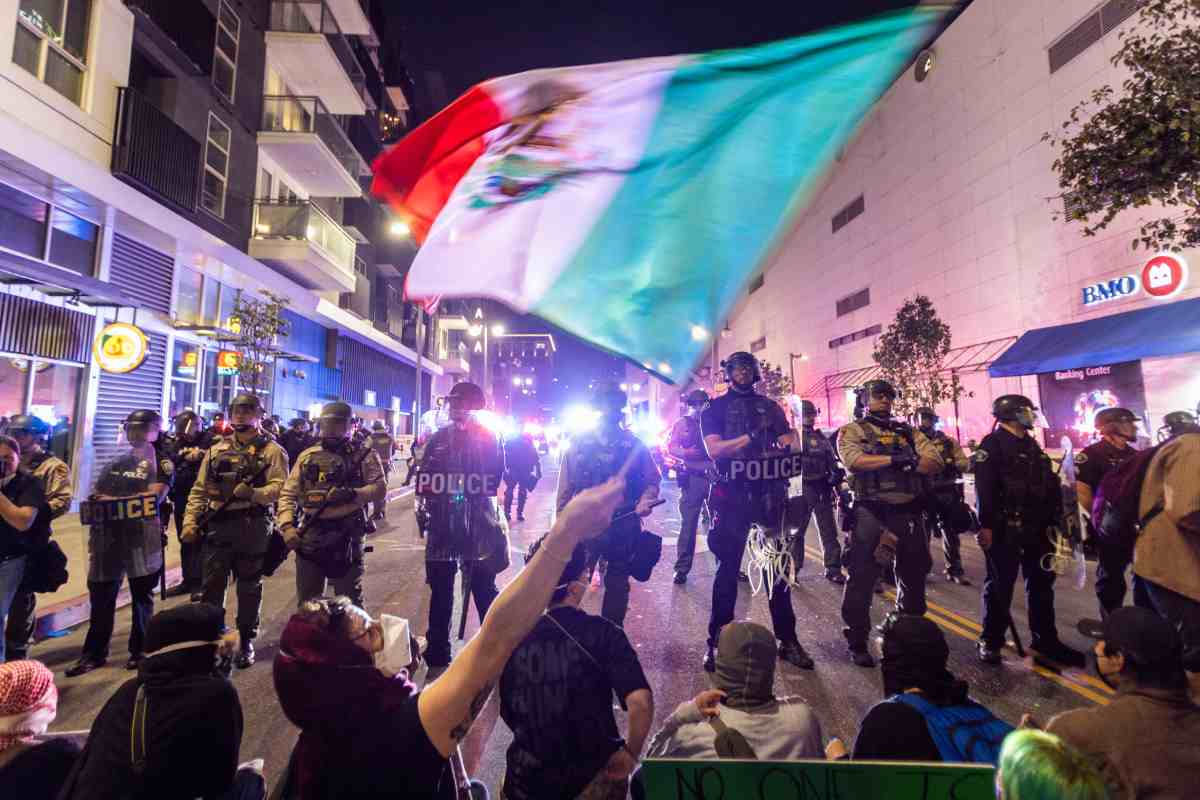 Manifestantes ondean una bandera de México frente a la barricada de policías durante las protestas contras las redadas migratorias en Los Ángeles
