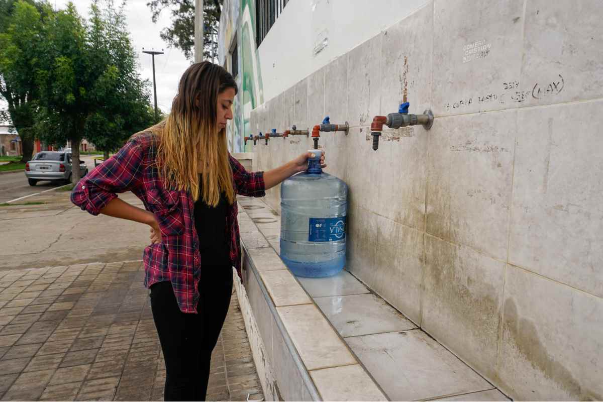 Valentina Adrover, de 24 años, llena un bidón de agua en una canilla pública en Nueve de Julio. Mientras persisten las dudas sobre el suministro de agua potable a los hogares, los vecinos dependen cada vez más de los puntos de acceso públicos para contar con agua para beber y cocinar. Foto: Lucila Pellettieri, GPJ Argentina